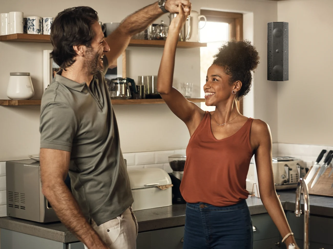 A couple dancing in their kitchen with a Lithe Audio speaker on the wall behind them
